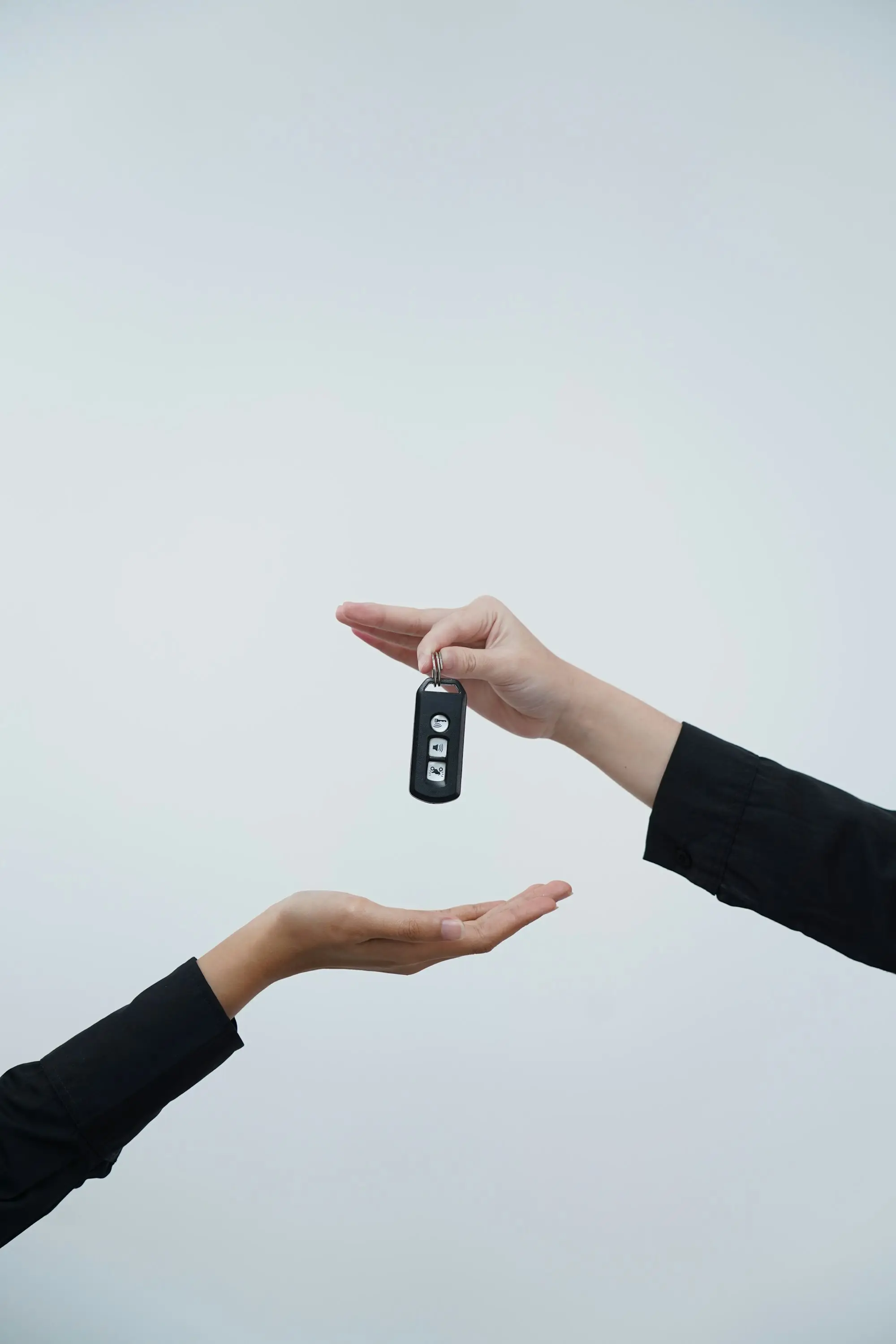 Hands exchanging a car key against a light background.
